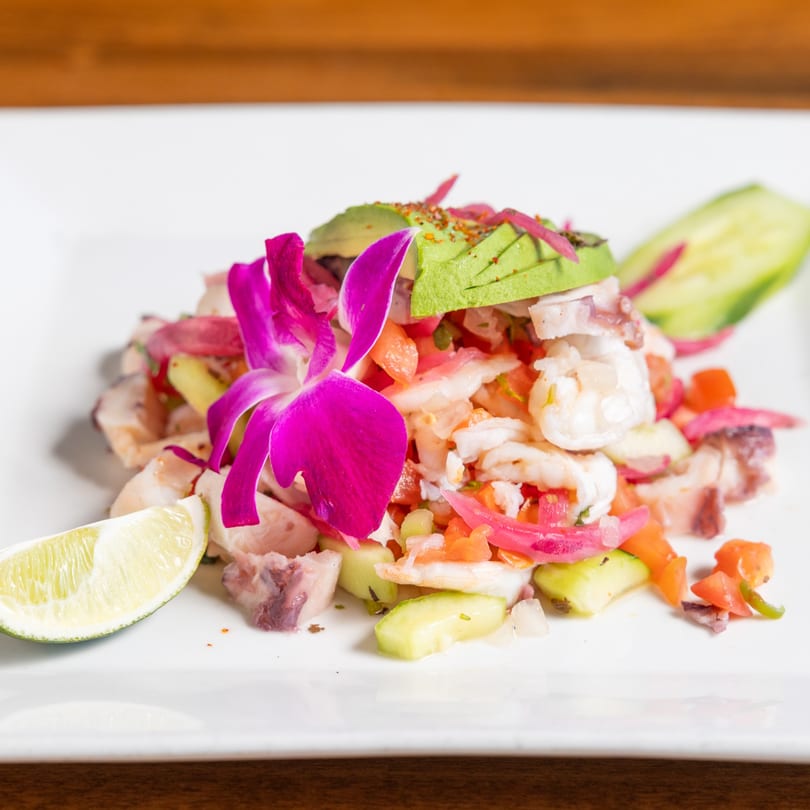 Mexican ceviche with shrimp, octopus, avocado, red onion, cucumber, and a purple orchid garnish.