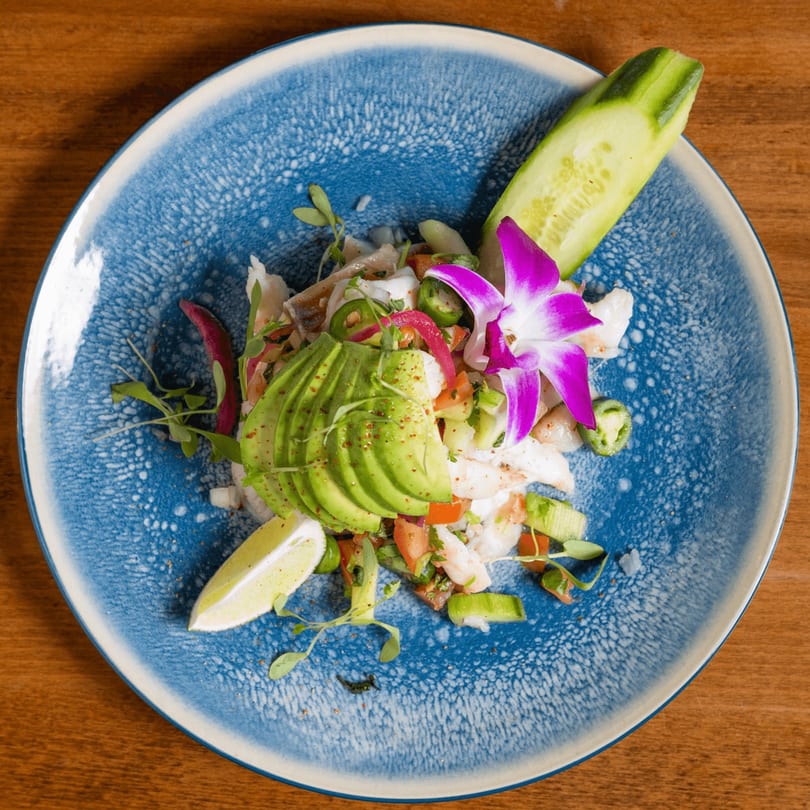 California Tacos Cantina and Distillery's ceviche with avocado, lime, cucumber, and a purple orchid on a blue plate.
