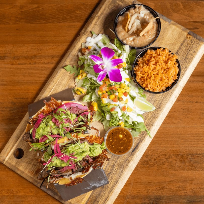 Mexican steak taco with guacamole, pickled onions, rice, beans, and salad on a wooden board.