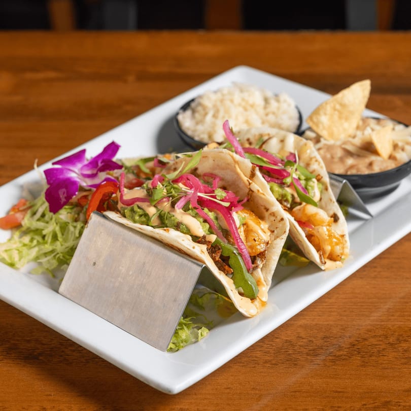 Two California Tacos with rice, chips, and dip, garnished with a purple orchid.